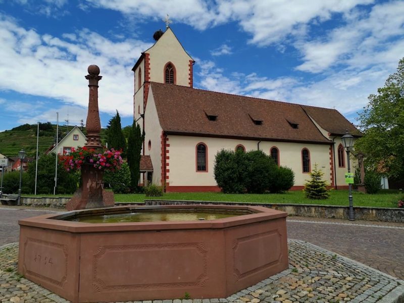 Brunnen vor Kirche mit Storchennest auf dem Kirchturm