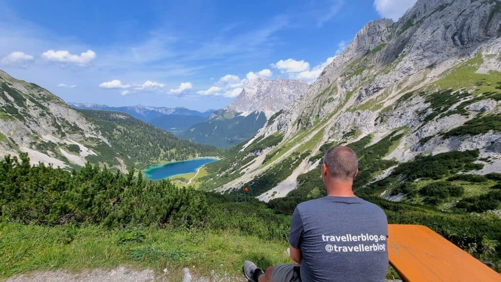 Hubert Mayer vom Travellerblog.eu auf einer Bank auf dem Berg mit Blick auf die Berge und dem Seebensee bei strahlend blauen Himmel