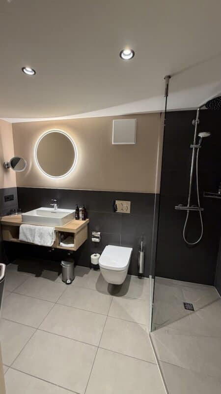 Badezimmer mit Waschbecken, rundem Spiegel, Toilette und Dusche